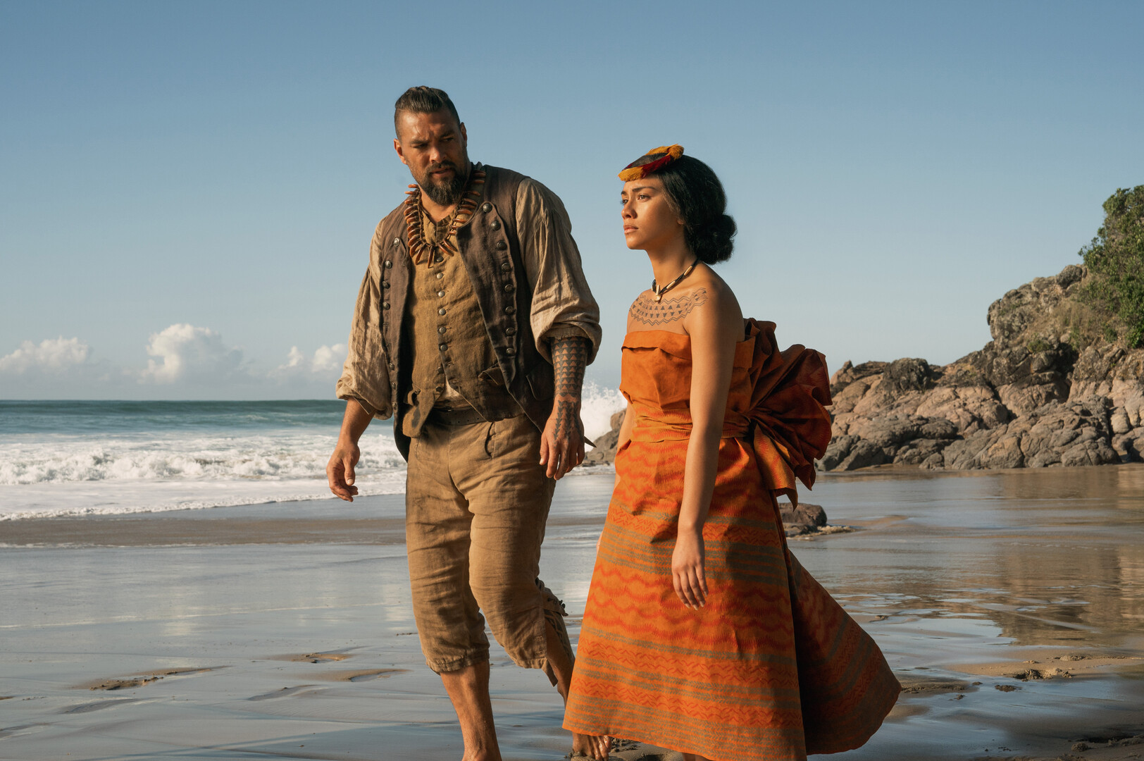 Jason Momoa walking on a beach with a female lead actor