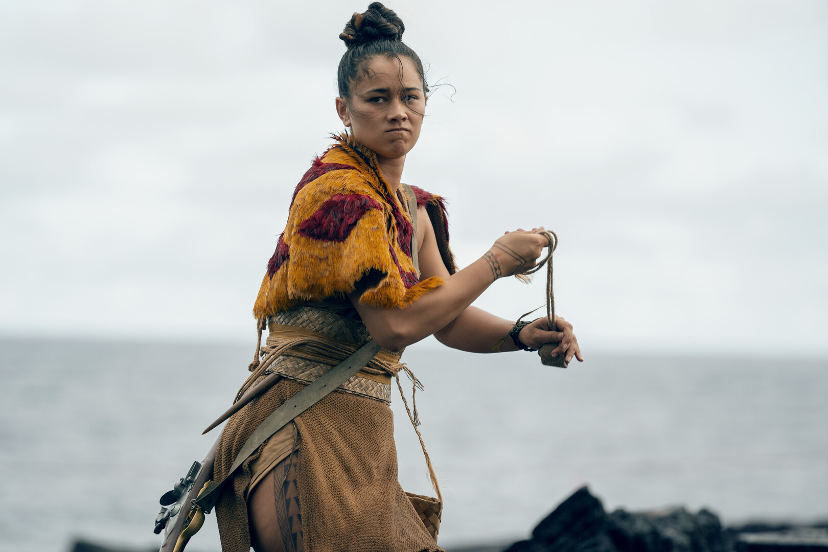 a woman on the beach in traditional Hawaiian dress with a musket slung over her shoulder