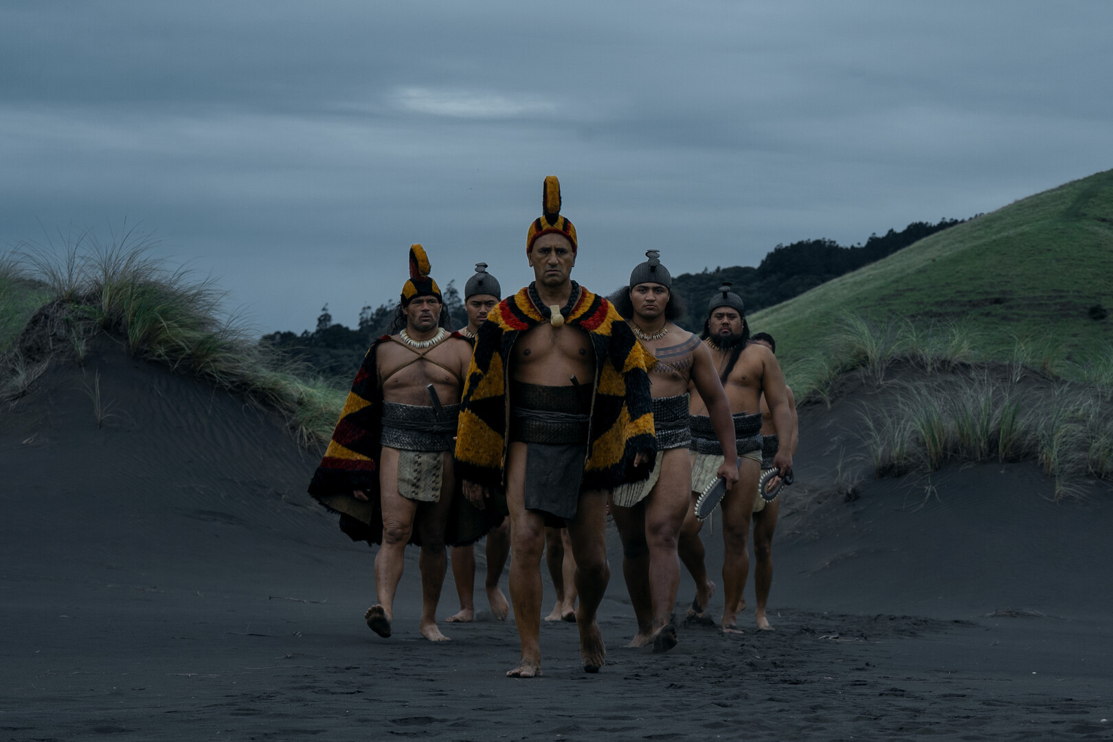tribal leaders walking toward camera over volcanic sand