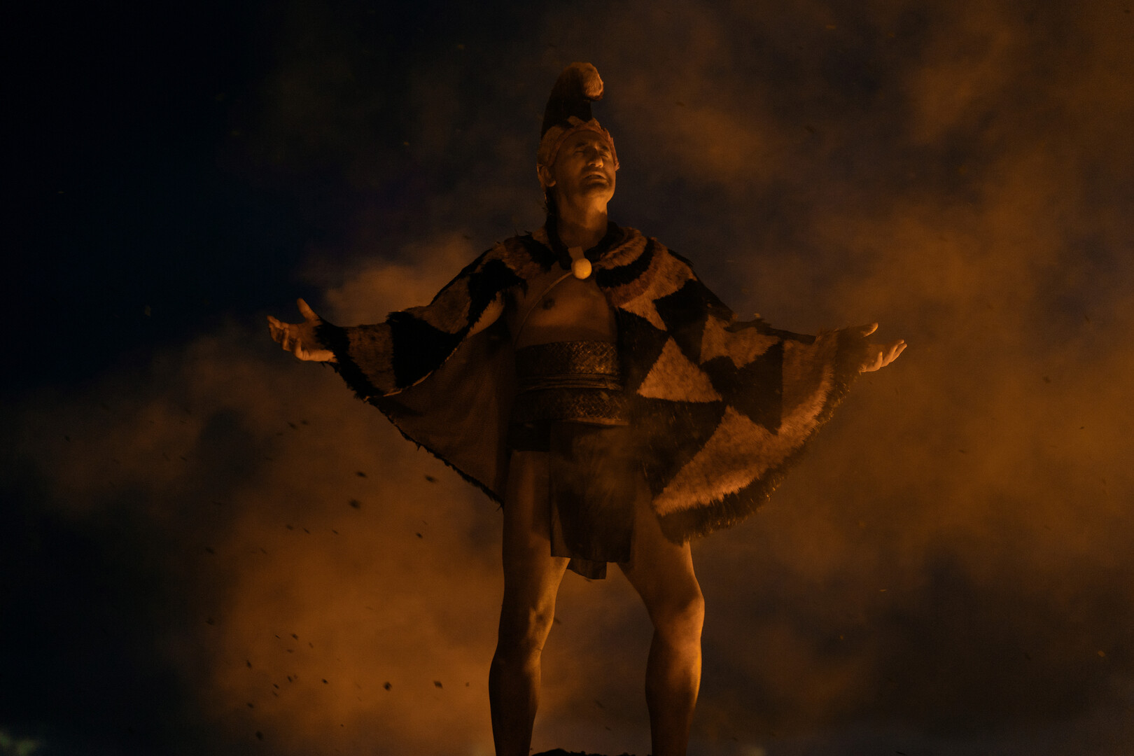 a tribal leader stands in front of a cloud of smoke at night