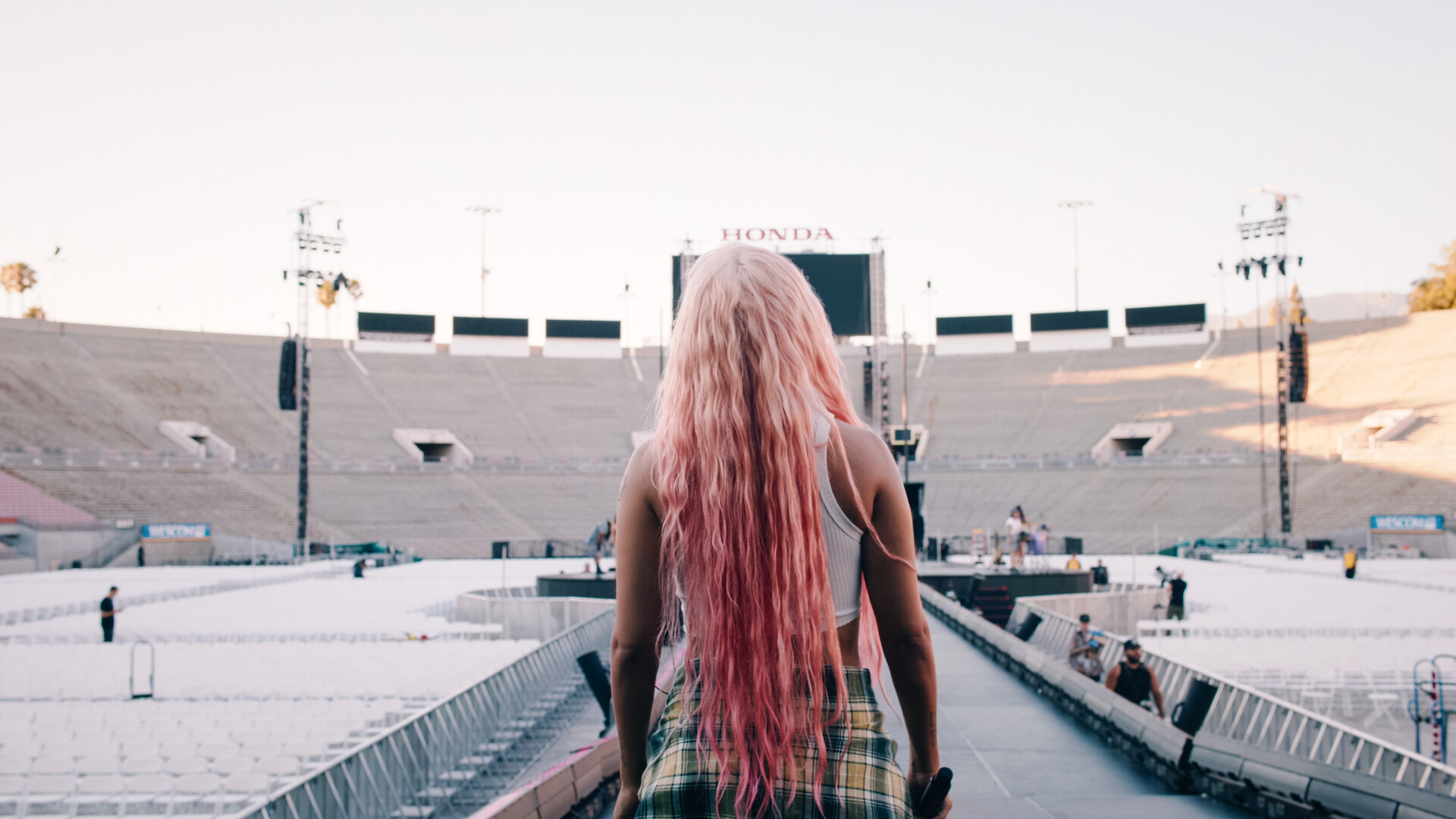 Karol G facing away from camera with an empty stadium in the background